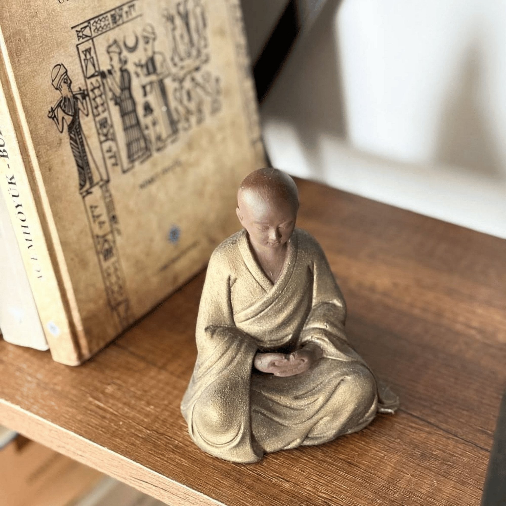 Bohem dekor tarzında bir kitaplık üzerinde sergilenen Zen heykeli. Uzak Doğu ve Asya kültürlerinden ilham alan el yapımı spiritüel figür, minimalist ve huzurlu bir atmosfer yaratıyor. Meditasyon, içsel denge ve boho dekor için ideal antik replika.