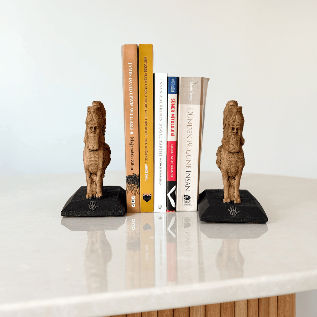 İki adet Lamassu heykelinin kitaplık bookend olarak kullanıldığı bu görselde, figürler kitapların iki yanına yerleştirilmiş ve koruyucu bir simetri oluşturmuştur. Asur tapınak kapılarına yerleştirilen Lamassular gibi bu düzenleme de sembolik bir koruma sağlar. Dekoratif, işlevsel ve tarihsel anlamlar taşıyan bu kompozisyon, koleksiyonluk heykeller arasında benzersizdir.