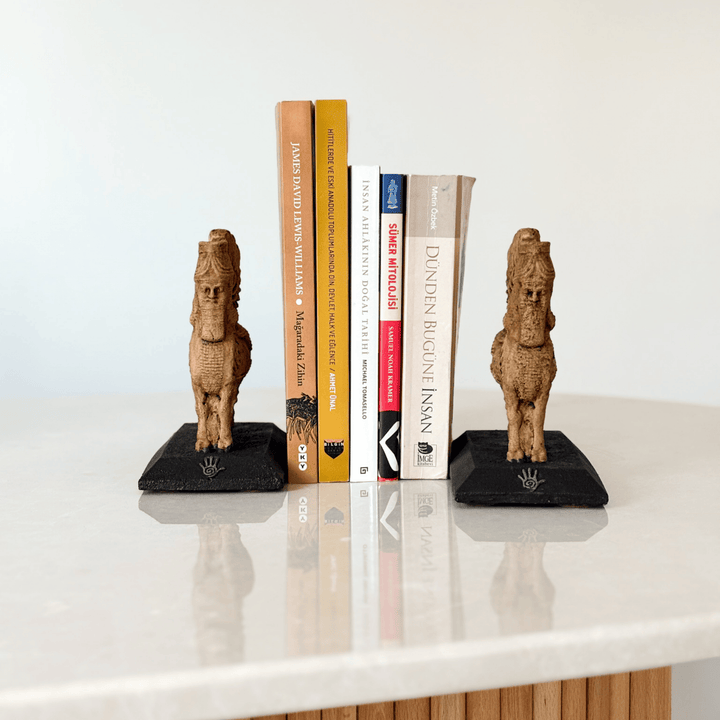 İki adet Lamassu heykelinin kitaplık bookend olarak kullanıldığı bu görselde, figürler kitapların iki yanına yerleştirilmiş ve koruyucu bir simetri oluşturmuştur. Asur tapınak kapılarına yerleştirilen Lamassular gibi bu düzenleme de sembolik bir koruma sağlar. Dekoratif, işlevsel ve tarihsel anlamlar taşıyan bu kompozisyon, koleksiyonluk heykeller arasında benzersizdir.