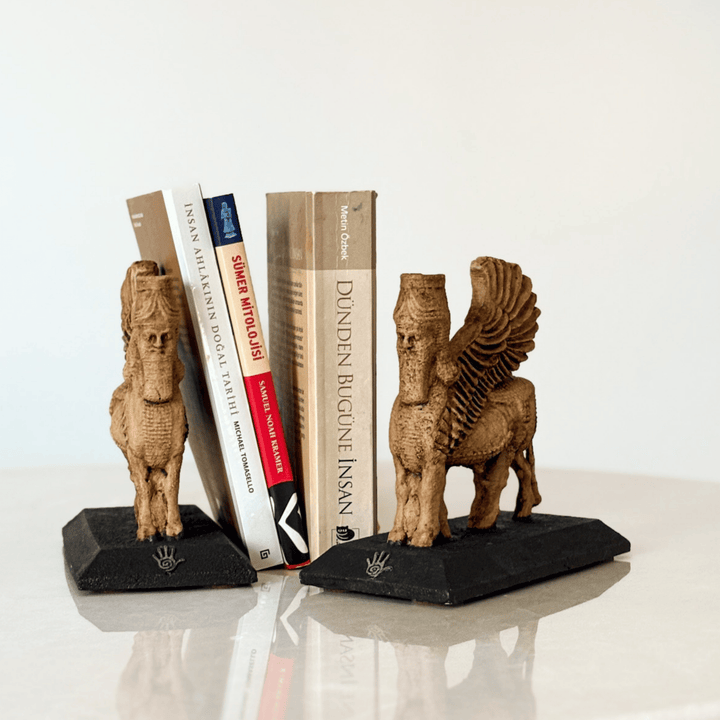 İki adet Lamassu heykelinin kitaplık bookend olarak kullanıldığı bu görselde, figürler kitapların iki yanına yerleştirilmiş ve koruyucu bir simetri oluşturmuştur. Asur tapınak kapılarına yerleştirilen Lamassular gibi bu düzenleme de sembolik bir koruma sağlar. Dekoratif, işlevsel ve tarihsel anlamlar taşıyan bu kompozisyon, koleksiyonluk heykeller arasında benzersizdir.
