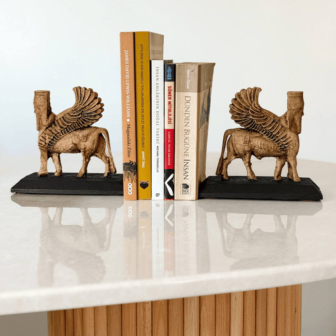 İki adet Lamassu heykelinin kitaplık bookend olarak kullanıldığı bu görselde, figürler kitapların iki yanına yerleştirilmiş ve koruyucu bir simetri oluşturmuştur. Asur tapınak kapılarına yerleştirilen Lamassular gibi bu düzenleme de sembolik bir koruma sağlar. Dekoratif, işlevsel ve tarihsel anlamlar taşıyan bu kompozisyon, koleksiyonluk heykeller arasında benzersizdir.