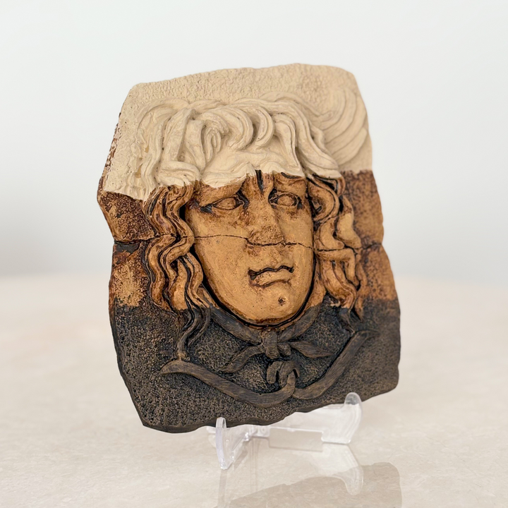 “Medusa relief sculpture showcased on a clear stand under warm natural sunlight, highlighting its fine texture and earthy tones. Perfect for boho, classic, or archaeological home decor themes.”
TR:
“Şeffaf stand üzerinde sıcak doğal güneş ışığı altında sergilenen Medusa rölyefi — ince dokusunu ve toprak tonlarını vurguluyor. Boho, klasik veya arkeolojik ev dekoru temaları için mükemmel.”