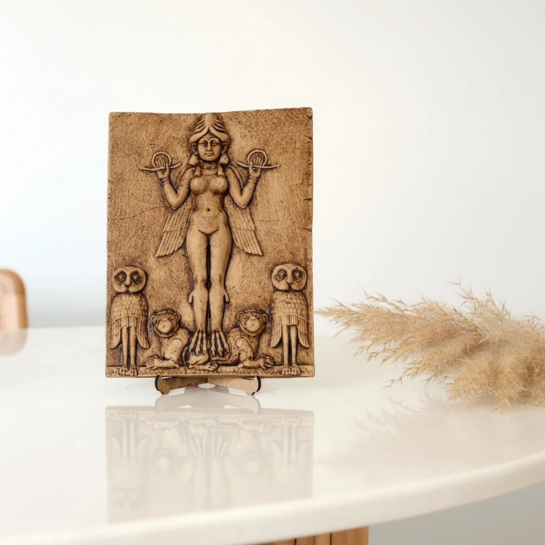 Gecenin Kraliçesi rölyefi masa üzerinde sergilenen dekoratif ürün fotoğrafı. Mezopotamya sanatının ünlü Burney Relief kabartmasından ilham alınarak üretilmiş Queen of the Night relief heykeli, çalışma masasında kitap ve dekoratif objelerle birlikte sergilenmektedir. ArkeoArt tarafından üretilen bu Mezopotamya tanrıça rölyefi replikası, antik Babil mitolojisini temsil eden koleksiyonluk bir arkeoloji ve mitoloji sanat objesidir.