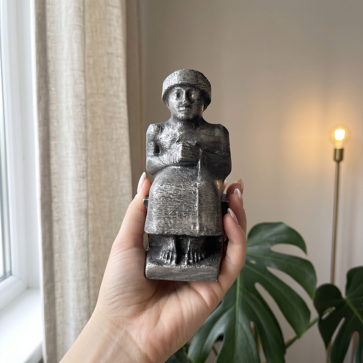 Kadın elinde tutularak ürünün gerçek boyutunu gösteren fotoğraf. Gudea Heykeli Replikası, tek elde rahatlıkla kavranabilecek ölçüleriyle diorit taş görünümünü, ince yüzey dokusunu ve üzerindeki karakteristik Sümer çivi yazısı detaylarını yakından sergiler. Lagaş Kralı Gudea'yı temsil eden bu Neo Sümer müze replikası; Antik Mezopotamya tarihi, arkeoloji ve koleksiyon dekorasyonu tutkunları için ArkeoArt el işçiliğiyle hazırlanmış seçkin bir sanat eseridir.