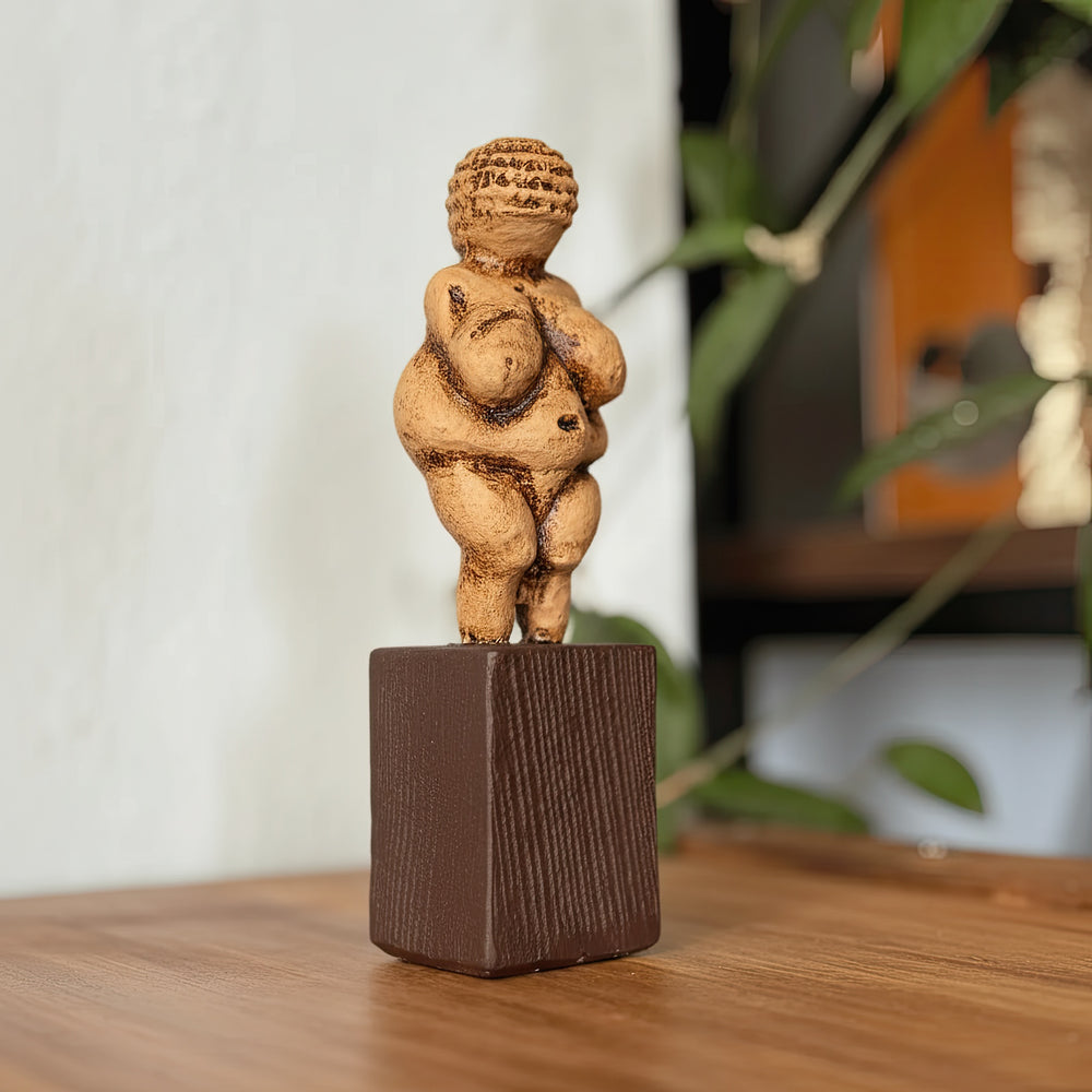Willendorf Venüsü replikası masa üzerinde çapraz açıdan çekilmiş ana ürün fotoğrafı. Paleolitik dönemin ünlü Venus of Willendorf figüründen ilham alınarak hazırlanmış bu doğurganlık tanrıçası heykeli, antik taş dokusunu yansıtan patina yüzeyiyle sergilenmektedir. ArkeoArt tarafından üretilen Paleolithic Venus statue replica, arkeoloji ve tarih koleksiyonları için müze tarzı bir tarih öncesi sanat objesidir.