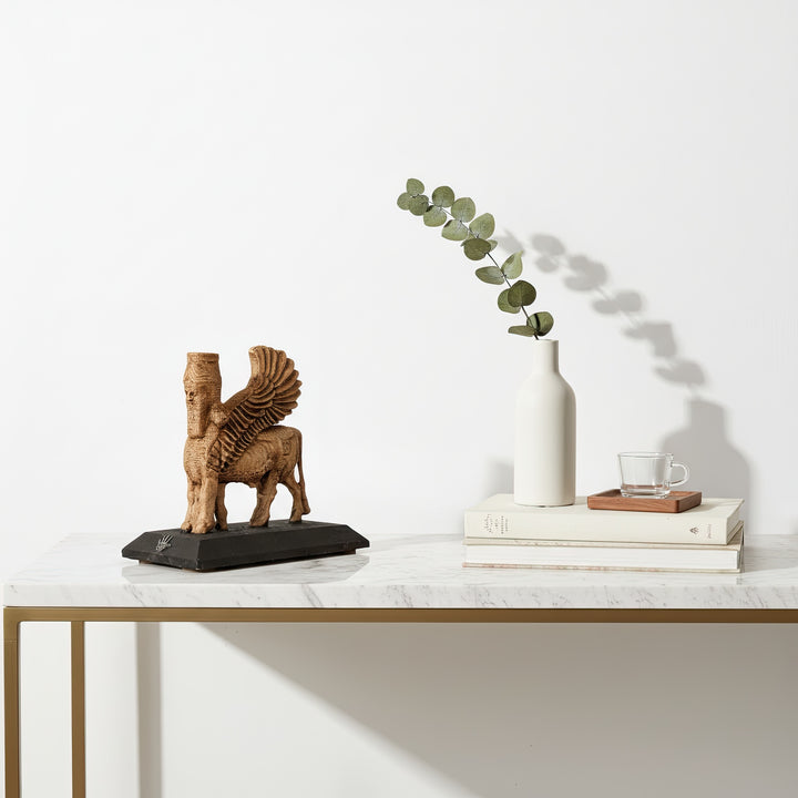 Üstten çekilmiş minimalist kompozisyonda Lamassu heykeli, yanında kitap ve bitki objeleriyle – fotoğraf sergilemeleri için etkileyici bir görüntü. / Top-view composition of Lamassu statue with books and plant – elegant archaeological art display for modern interiors and social showcases.